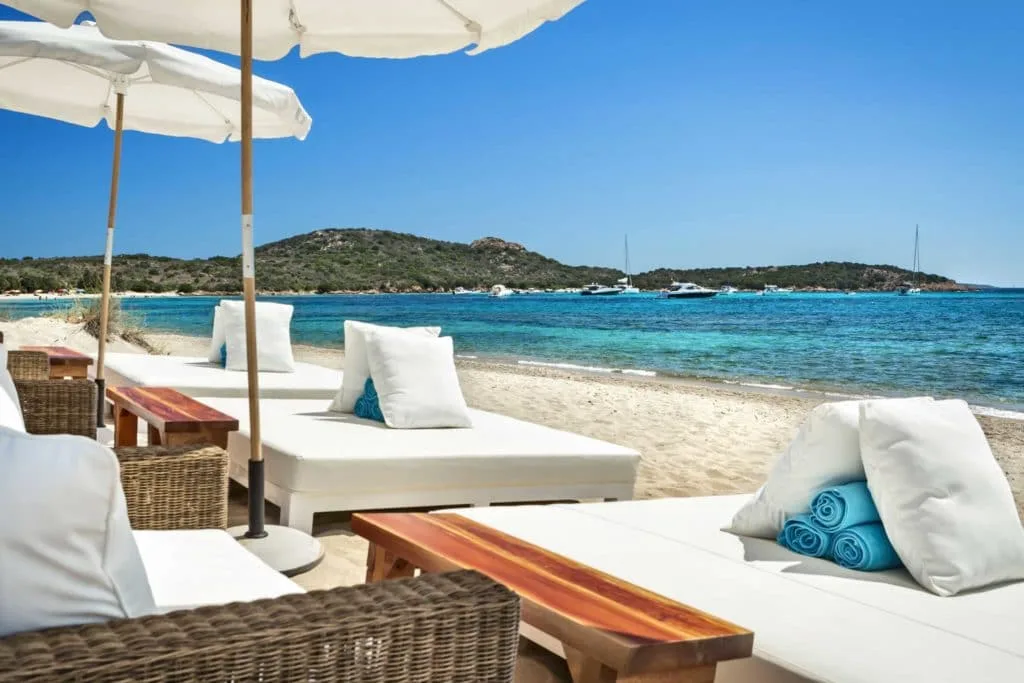 Rows of white daybeds in a sheltered cove at Nikki Beach, Cala Petra Ruja