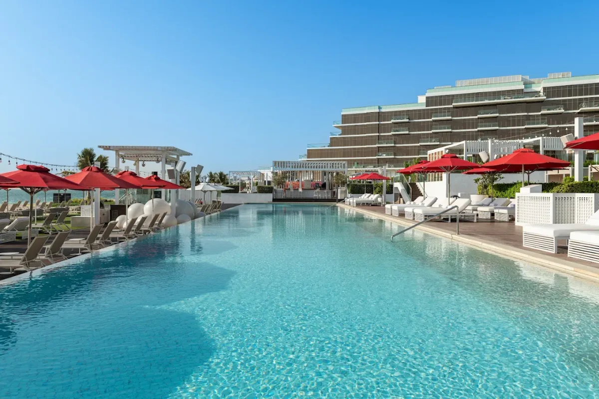 Infinity pool with white sunbeds and red parasols at Fluid Beach Club, TH8 Palm