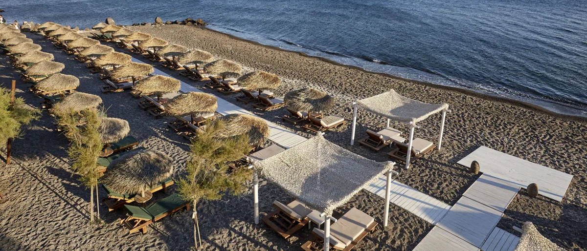 Lounge beds against volcanic cliffs at Theros Wave Bar, Vlychada