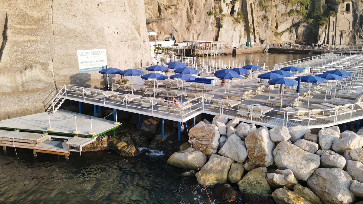 Wooden platforms and dark sand reached by a cliff lift at La Marinella Beach, Sant'Agnello